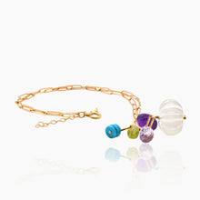 Load image into Gallery viewer, A gold paperclip chain bracelet featuring a cluster of colorful beads, including a large clear ribbed glass orb, a purple faceted bead, a blue bead, and a green bead, displayed on a reflective white surface.