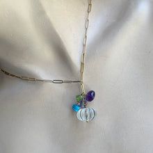 Load image into Gallery viewer, A gold paperclip chain necklace with a central cluster of colorful beads, including a clear ribbed glass bead, a purple bead, a green bead, and a blue bead, displayed on a beige fabric background.